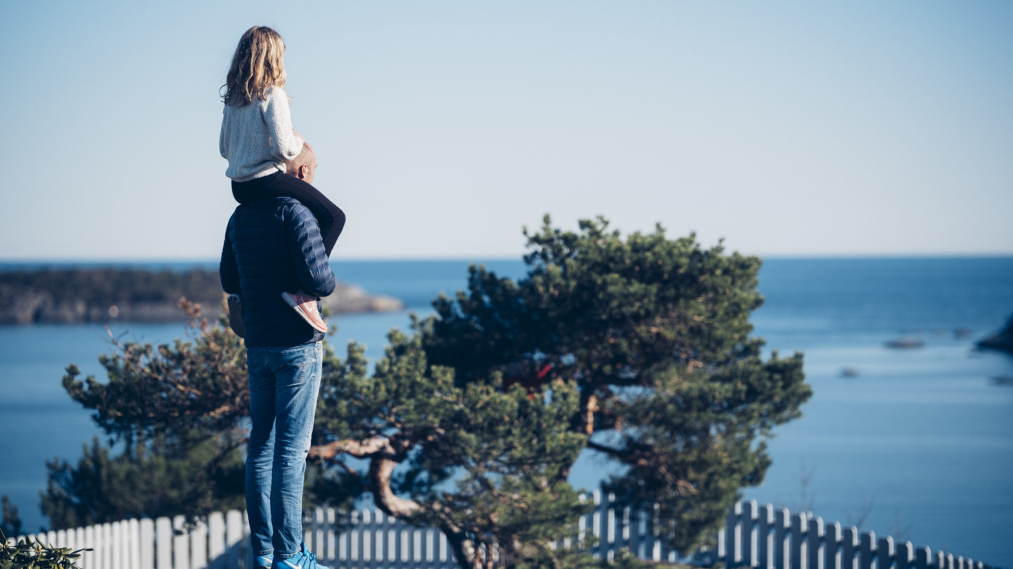 Jente sitter på skuldrene til en mann, ser utover fjorden i sollys.